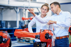Industrie-Fotografie: Poppe + Potthoff Image. Ein Mann und eine Frau stehen in einer modernen sauberen Produktion. Sie schauen sich kontrollierend ein Bauteil an, welches der Mann auf Augenhöhe hoch hält.